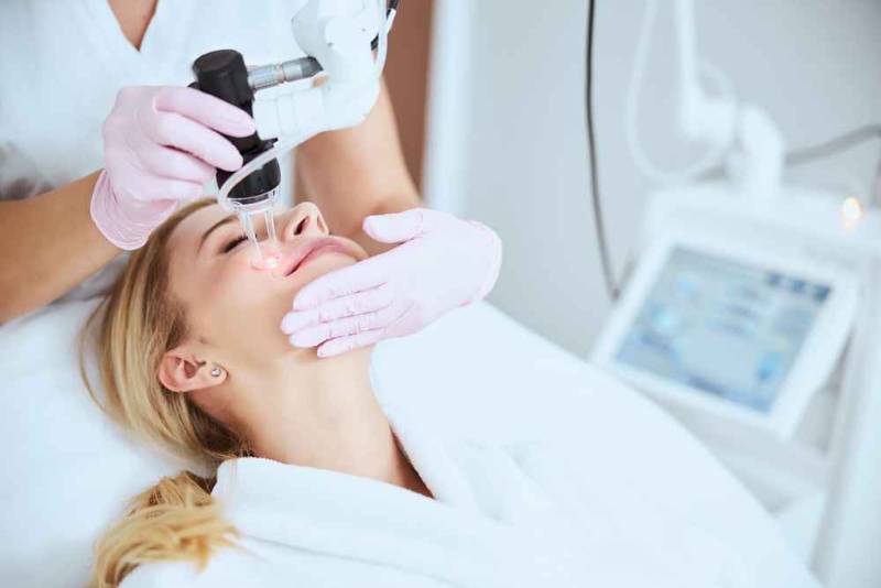 Dermatologist performing fractional laser treatment on a patient’s face in a clinic
