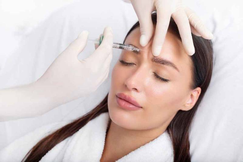 A woman receiving a Botox injection on her face from a professional in a clinical setting, focusing on wrinkle treatment and facial rejuvenation