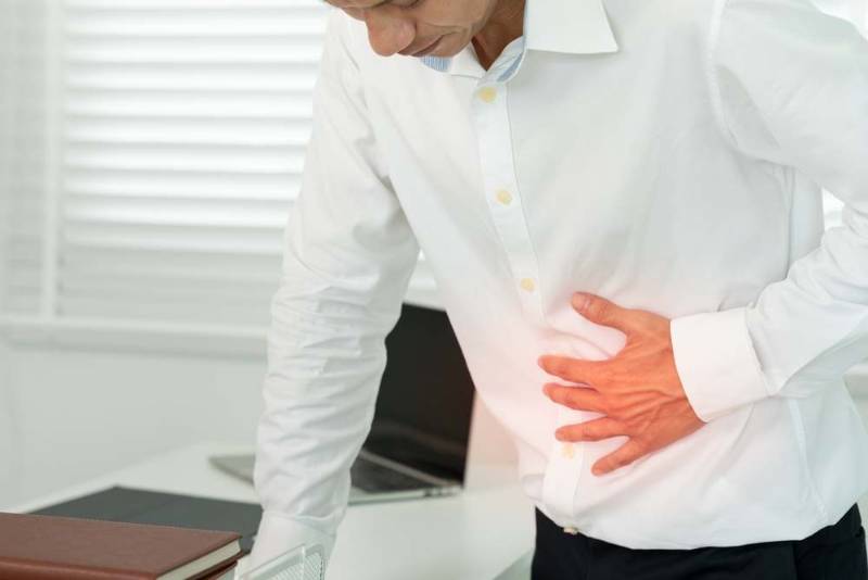 A person standing and pressing their stomach with both hands, appearing uncomfortable due to indigestion and bloating