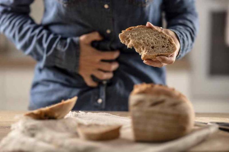 A person holding bread while clutching their abdomen in pain, symbolizing gluten intolerance and celiac disease