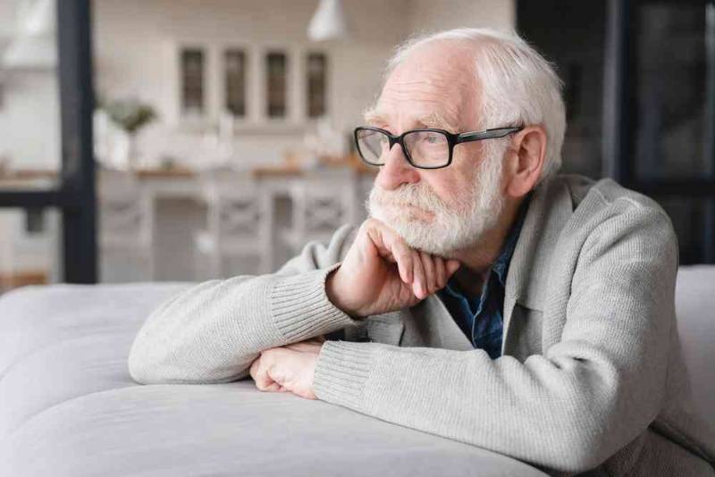 A lonely man sitting alone on a sofa, looking sad and isolated, representing social isolation