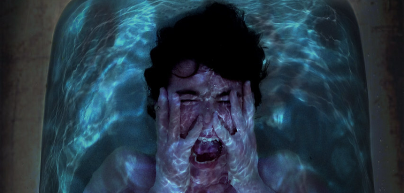 A distressed man crying and covering his face, overwhelmed by fear of water due to aquaphobia