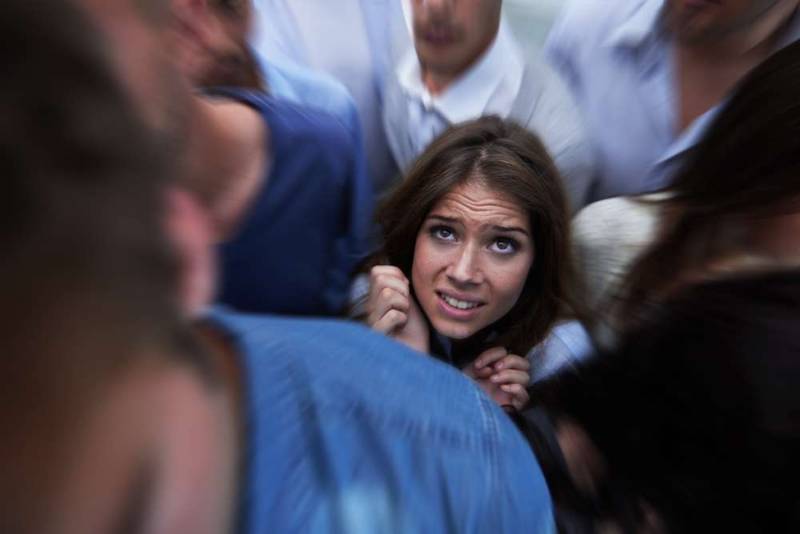 A young woman standing in a crowded place, looking anxious and distressed, showing signs of claustrophobia as she struggles with fear of confined spaces