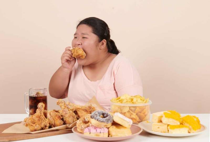 A woman sitting in front of a table filled with food, representing the struggle with binge eating disorder