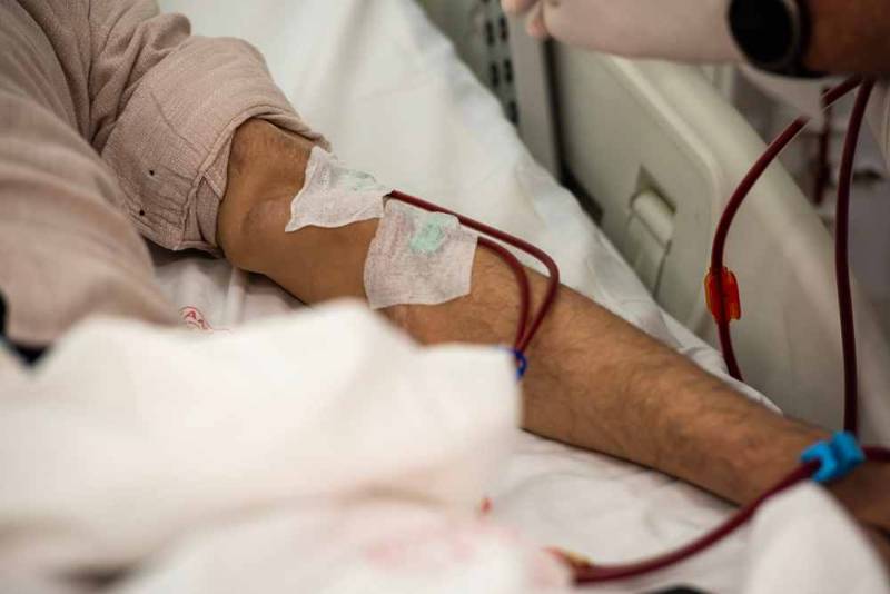 A patient sitting in a medical chair connected to a hemodialysis machine that filters blood through tubes
