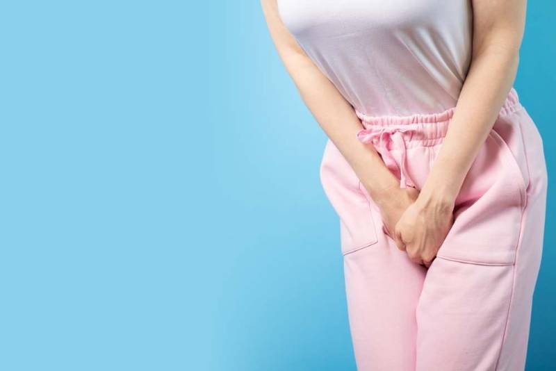 Photo of a woman holding her lower abdomen in discomfort, illustrating pain associated with urinary incontinence or bladder issues