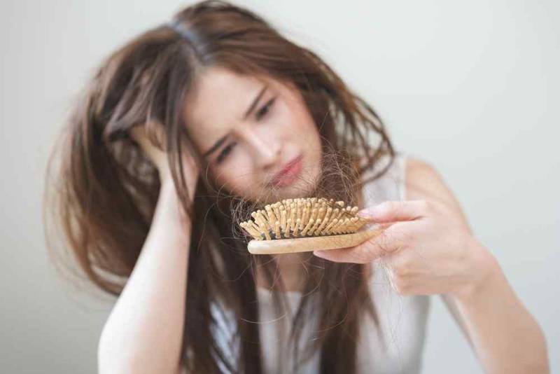 A worried woman looking at strands of hair collected in her brush, showing signs of hair loss
