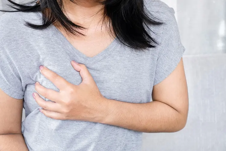A woman gently holding her breast with a pained expression, indicating discomfort or tenderness due to breast pain (mastalgia).